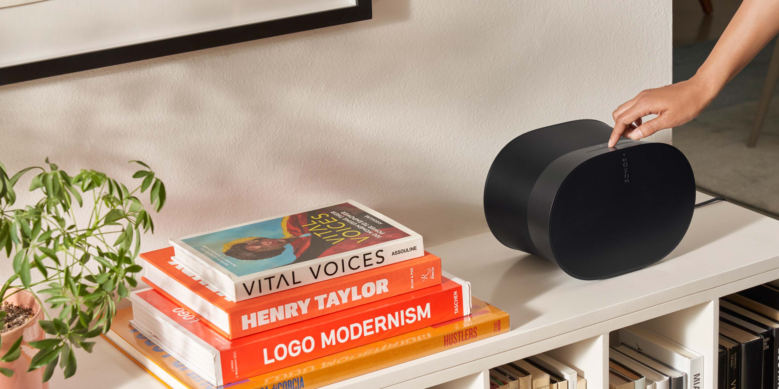 woman's hand adjusting a sonos speaker on a white table next to orange books