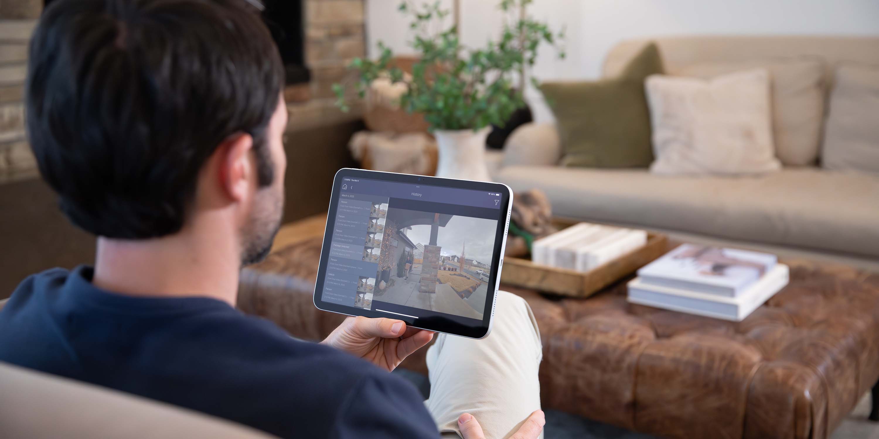a man holding a control4 touch panel looking at the surveillance screen in his living room